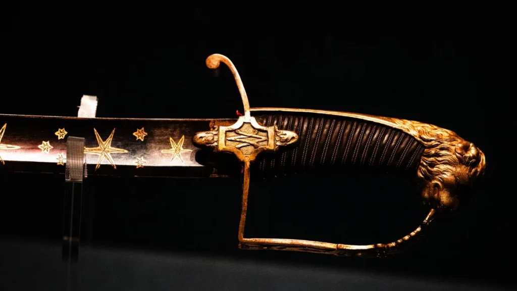 Sabre antigo com punho ornamentado exposto sobre fundo escuro