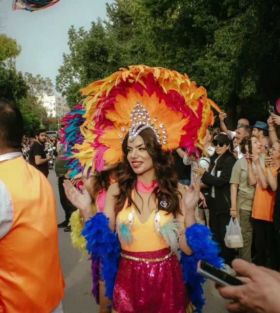 Desfile de carnaval em avenida, com integrante fantasiada e publico nas calcadas
