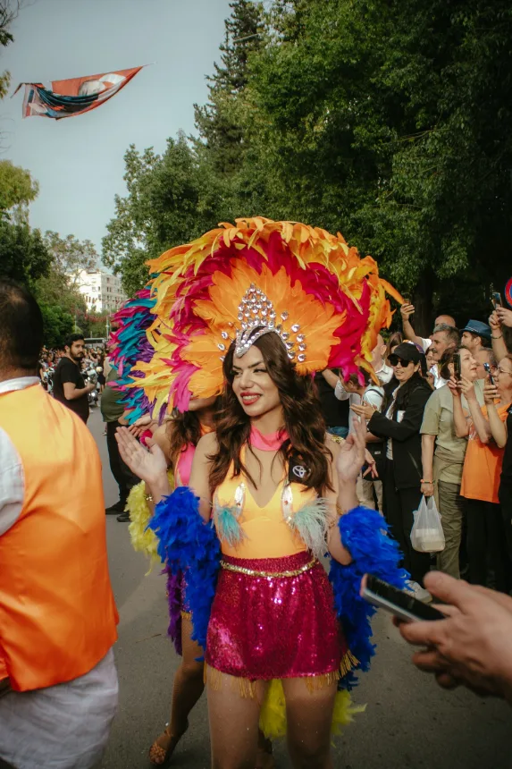 Desfile de carnaval em avenida, com integrante fantasiada e publico nas calcadas