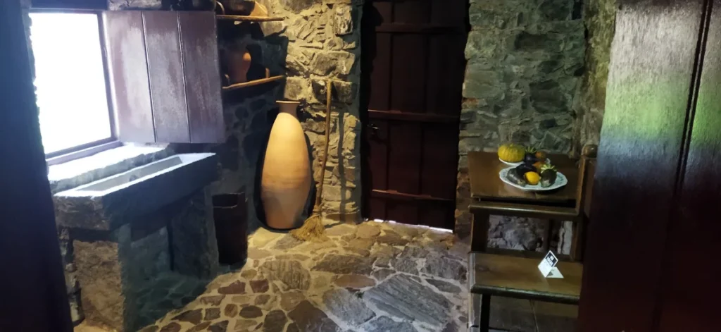 Cozinha com parede de pedra, jarro de barro e utensílios antigos