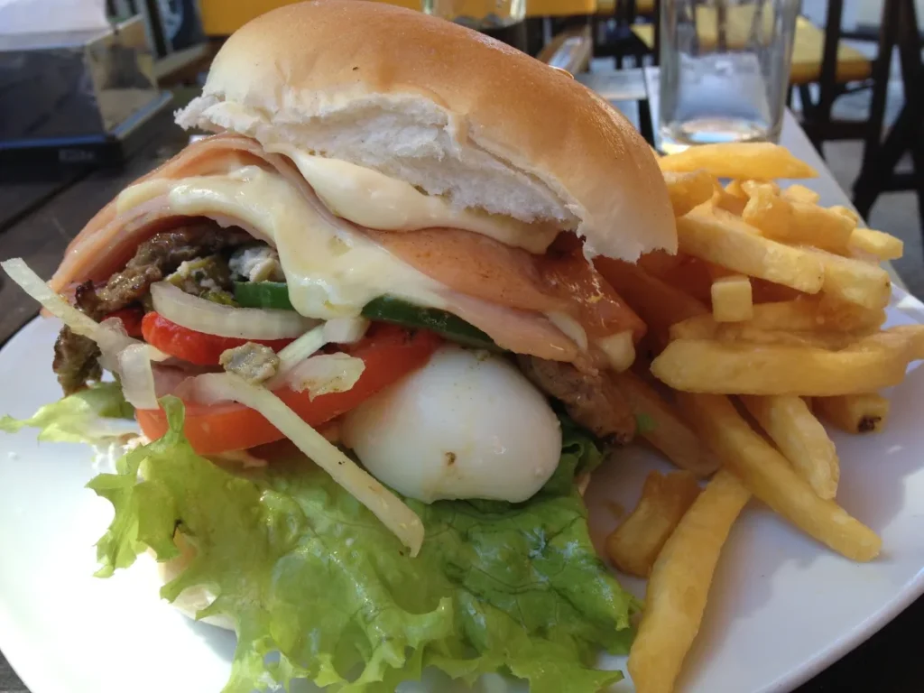 Chivito uruguaio servido no pao com batatas fritas ao lado, em prato de restaurante