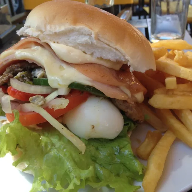 Chivito uruguaio servido no pao com batatas fritas ao lado, em prato de restaurante
