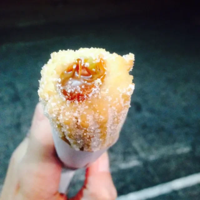 Churro uruguaio recheado servido no cone de papel, segurado na mao