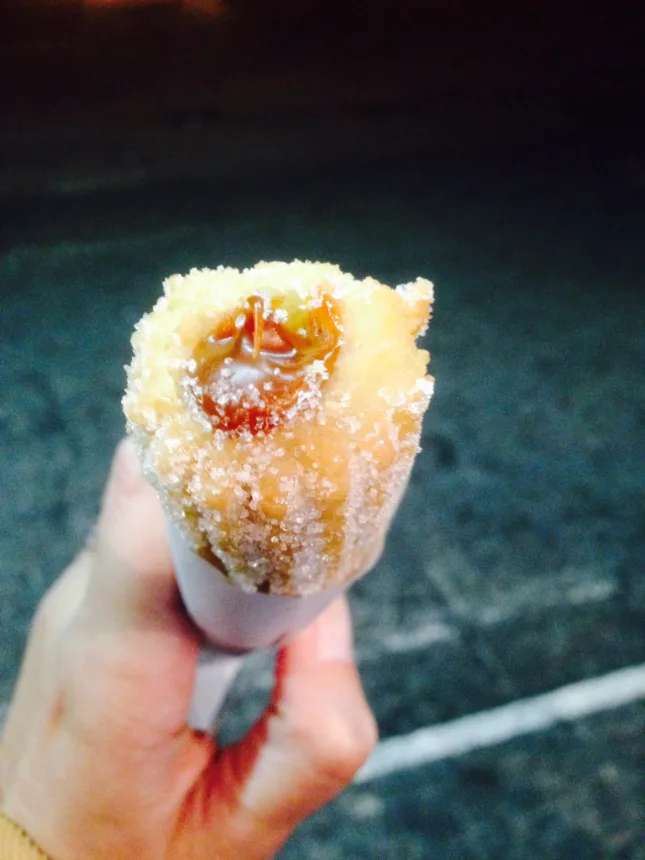 Churro uruguaio recheado servido no cone de papel, segurado na mao