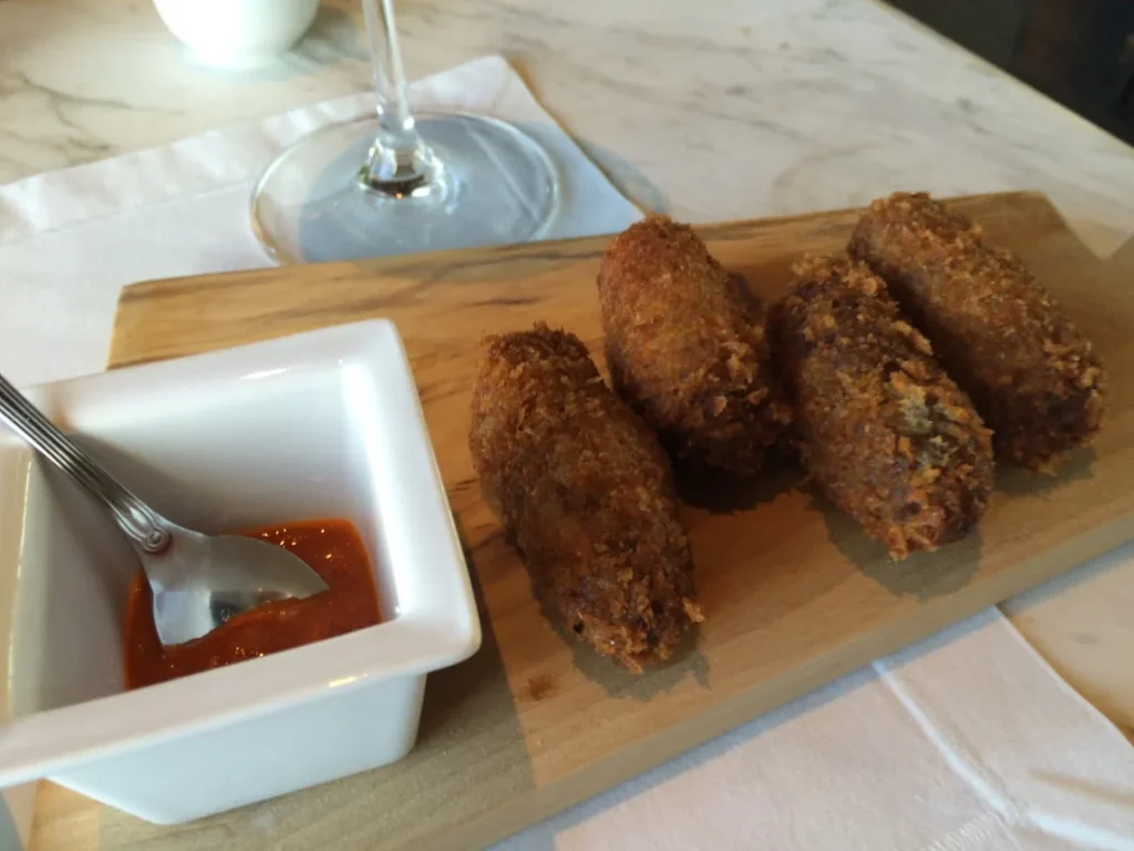 Croquetes servidos em tábua de madeira ao lado de uma taça de vinho