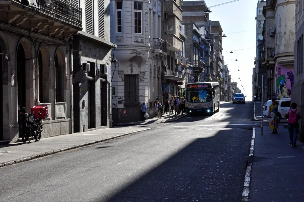 Rua do centro de Montevideo com onibus e pedestres entre predios antigos