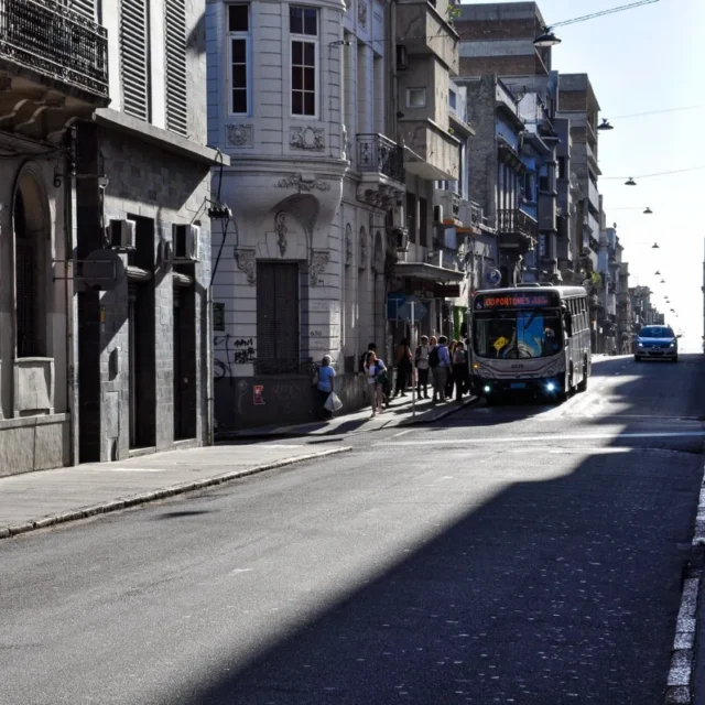 Rua do centro de Montevideo com onibus e pedestres entre predios antigos