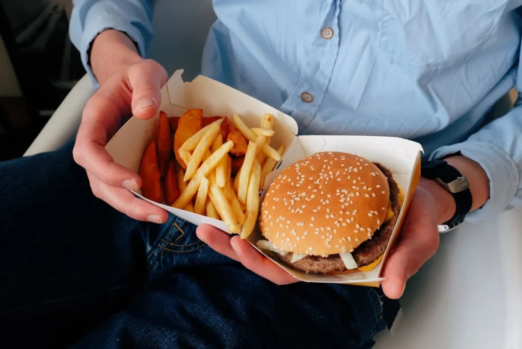 Maos segurando uma embalagem com hamburguer e batatas fritas na rua