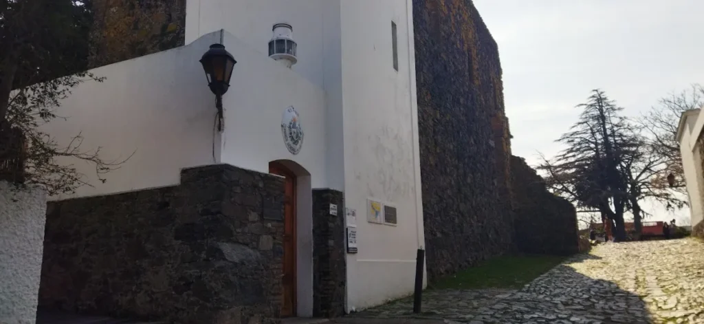 Parede caiada com lampião antigo ao lado da ruína de pedra do convento