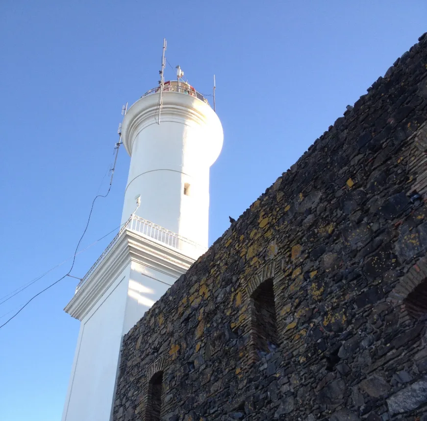 Torre branca do Farol de Colonia vista junto ao muro de pedra da ruína