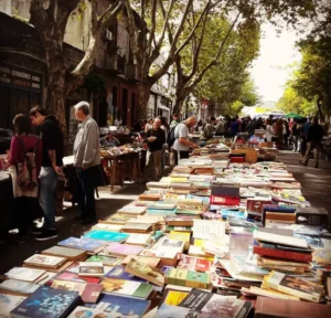 Rua arborizada tomada por barracas e livros espalhados no chao na feira Tristan Narvaja