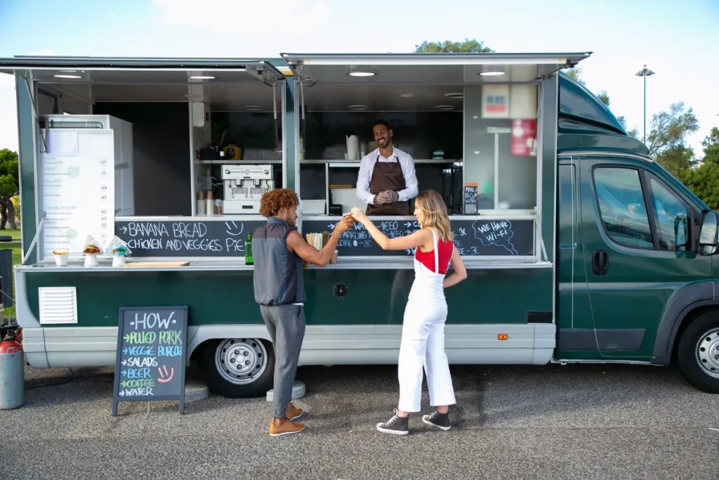 Food truck estacionado em area verde, com clientes fazendo o pedido no balcao