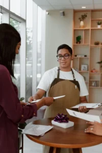 Atendente de avental entregando a conta a um cliente no balcão