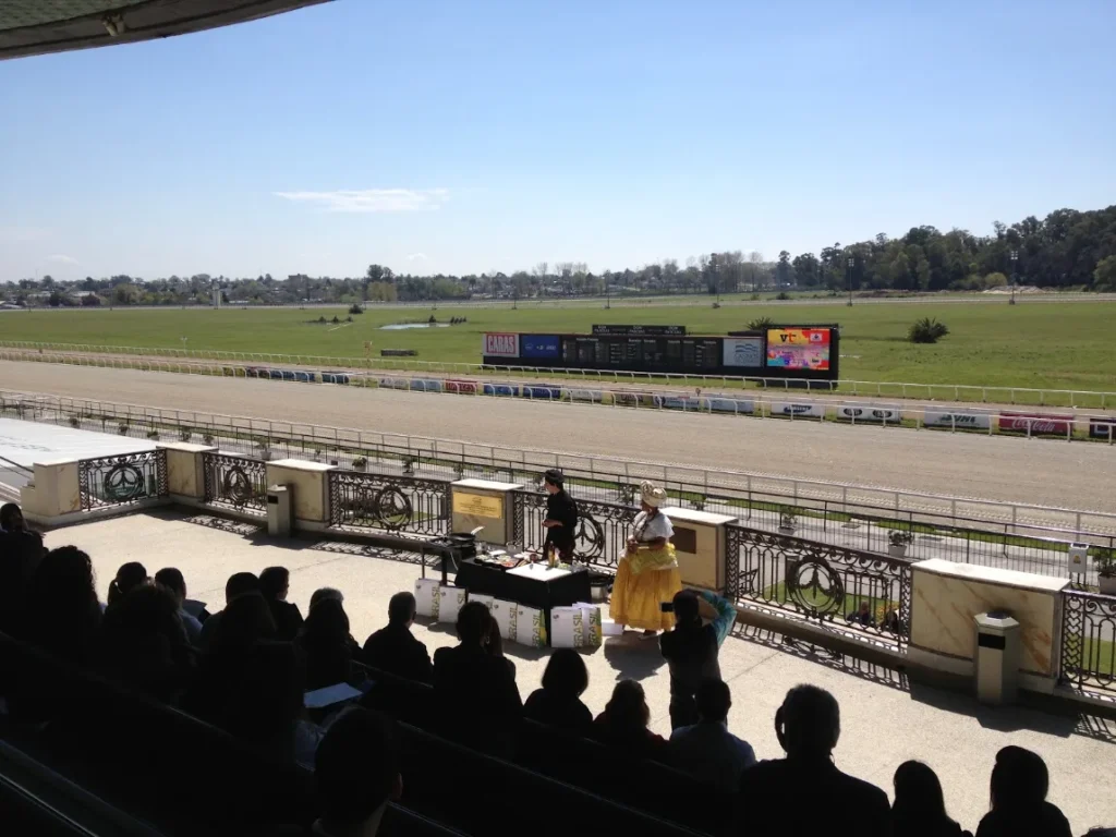 Público na arquibancada acompanhando a corrida na pista do hipódromo
