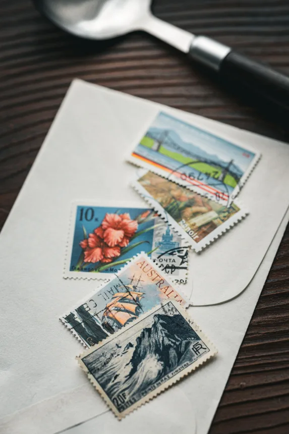 Envelope com selos postais e uma lupa sobre uma mesa de madeira