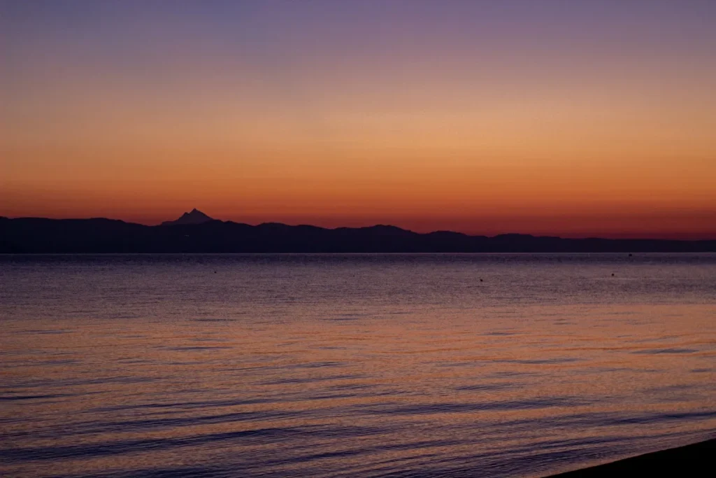 Entardecer sobre o mar com o horizonte alaranjado e o ceu ja escurecendo