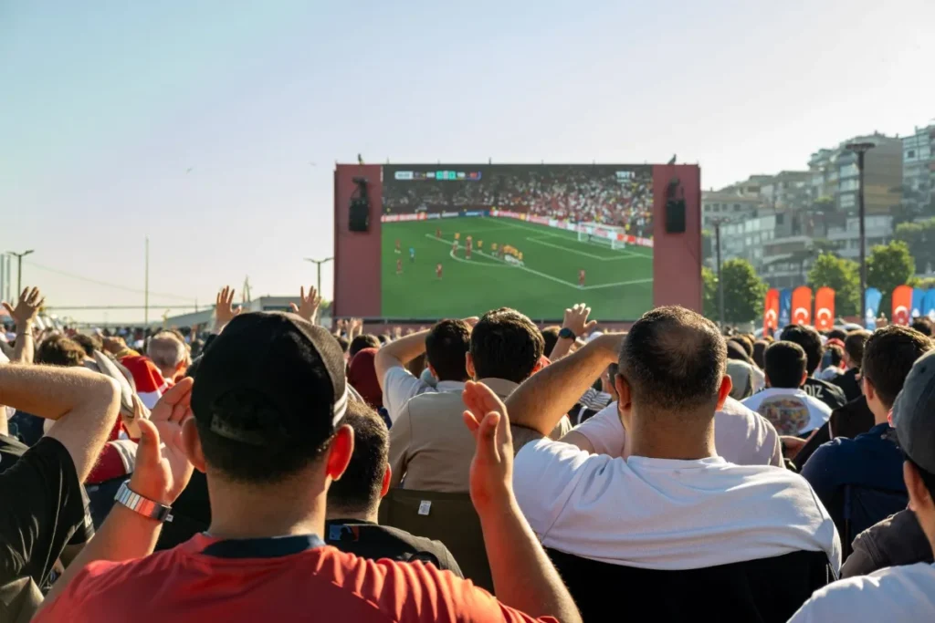 Multidao de torcedores assistindo a um jogo de futebol em telao ao ar livre