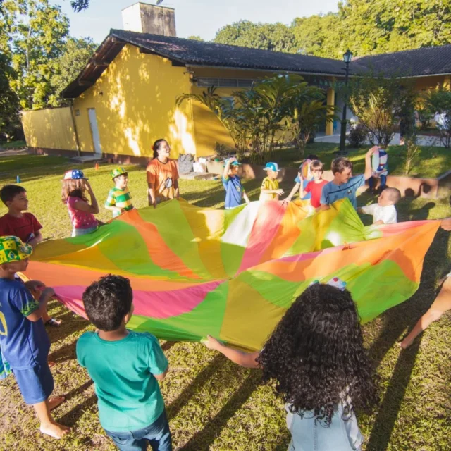 Criancas brincando ao ar livre com um paraquedas colorido em atividade recreativa