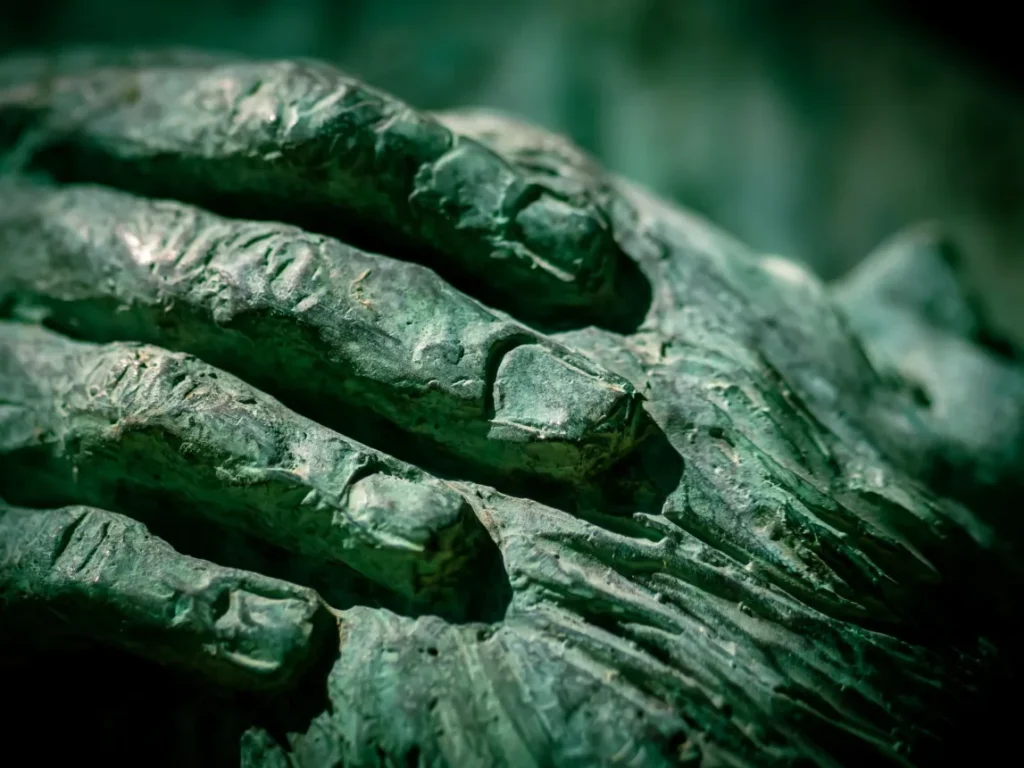 Detalhe de maos de uma escultura de bronze com patina esverdeada