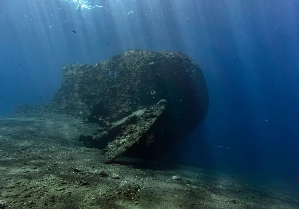 Casco de navio submerso em água escura atravessada por feixes de luz