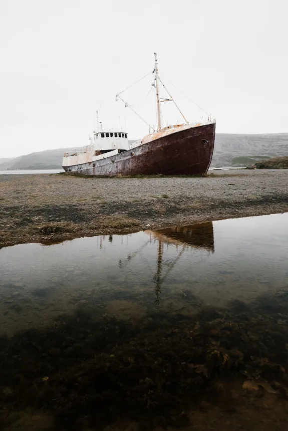 Navio encalhado em água rasa, refletido na superfície