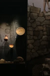 Peças de cerâmica iluminadas em vitrine ao lado de parede de pedra