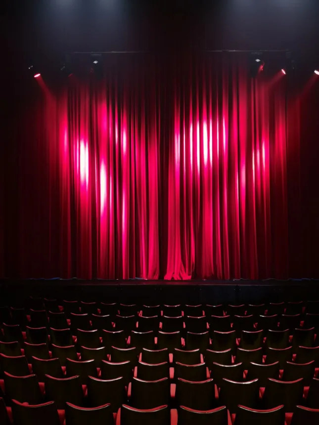 Palco com cortina vermelha e fileiras de poltronas vazias antes do espetaculo