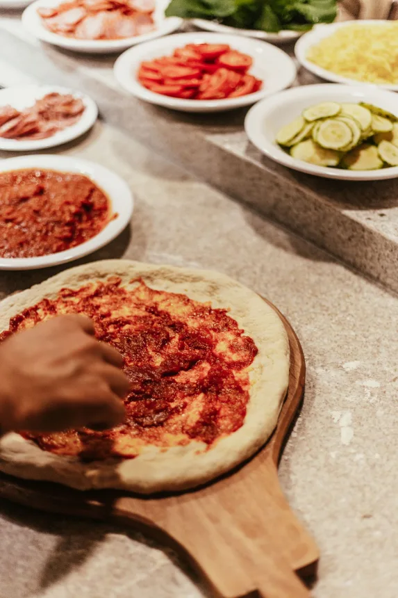 Mão espalhando molho de tomate sobre a massa de pizza na bancada