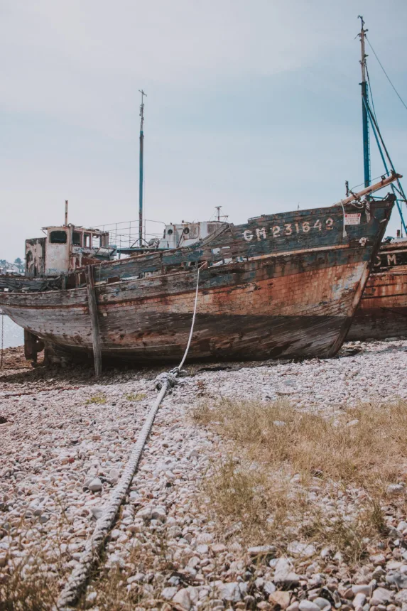 Casco de barco de madeira abandonado sobre a praia de pedras