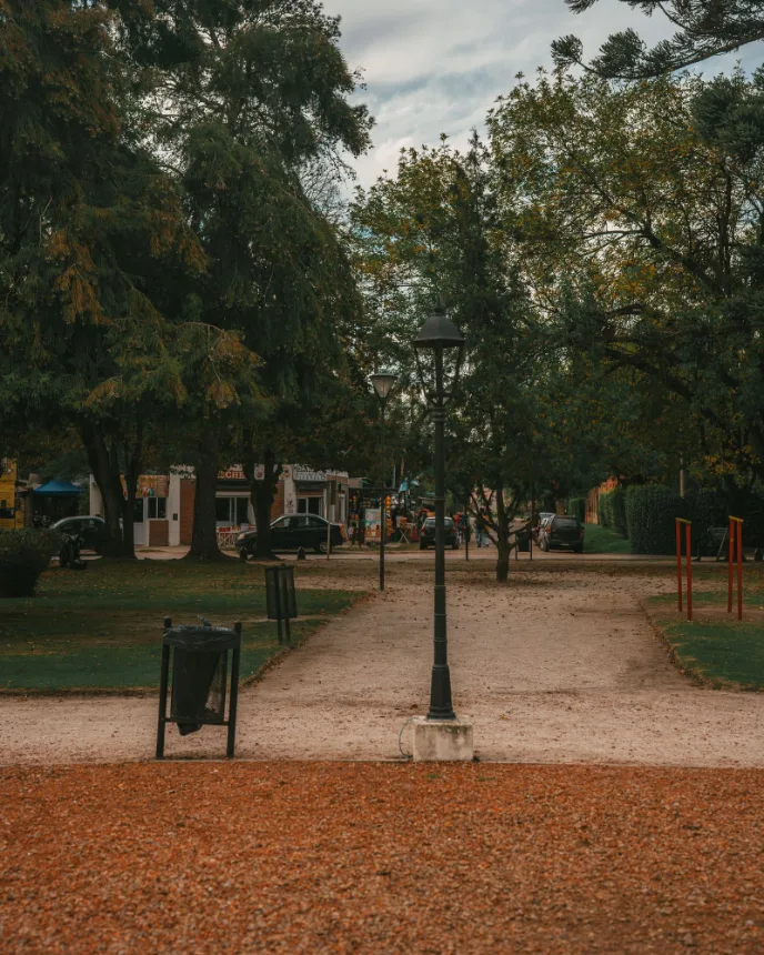 Caminho de terra em um parque arborizado com lampiao ao centro
