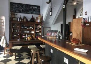 Interior de um aconchegante bar de vinhos com prateleiras de madeira para garrafas, cardápio em lousa e piso xadrez.
