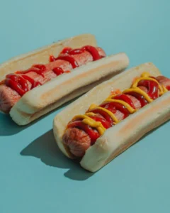 Dois panchos uruguaios com ketchup e mostarda sobre fundo azul