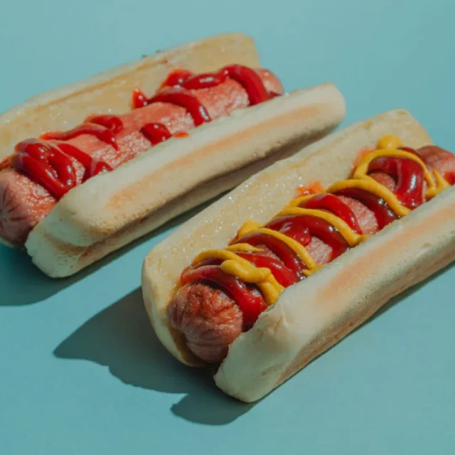Dois panchos uruguaios com ketchup e mostarda sobre fundo azul
