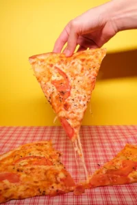 Fatia de pizza de muçarela com tomate vista de cima sobre fundo amarelo