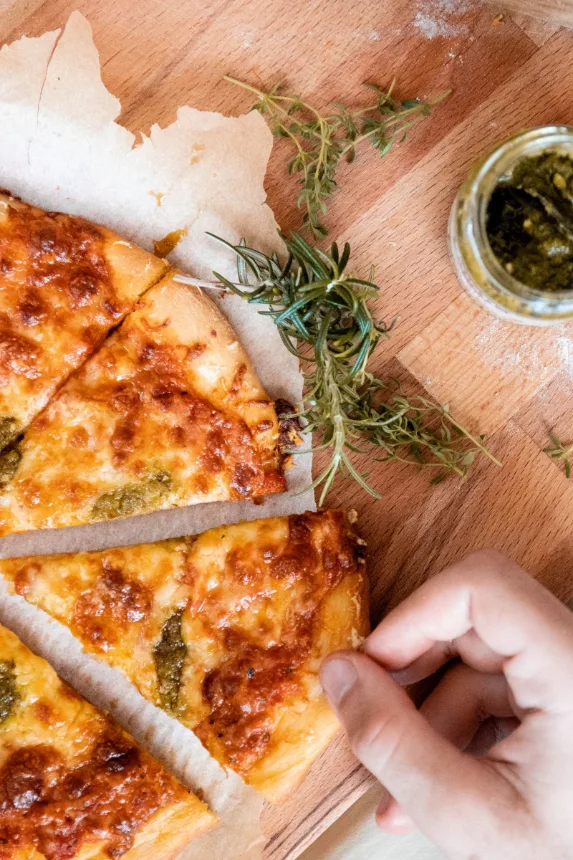 Fatias de pizza de queijo sobre tábua de madeira com alecrim ao lado