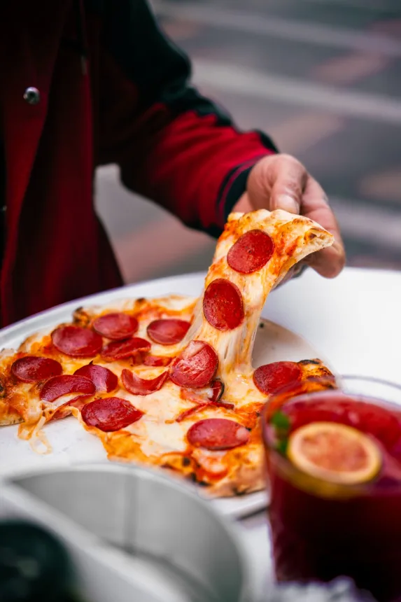 Fatia de pizza sendo levantada, com o queijo derretido esticando