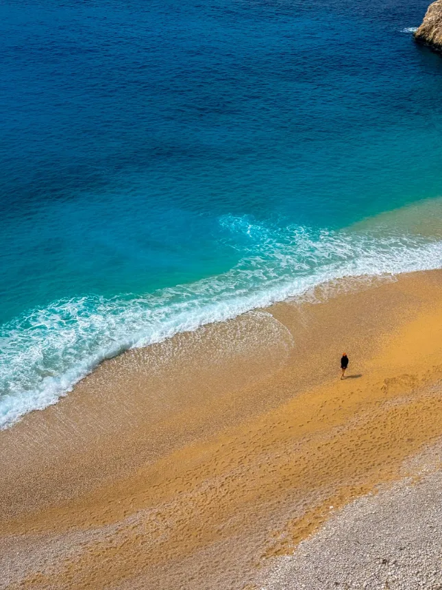 Praia de areia clara com mar calmo e uma pessoa caminhando a beira da agua