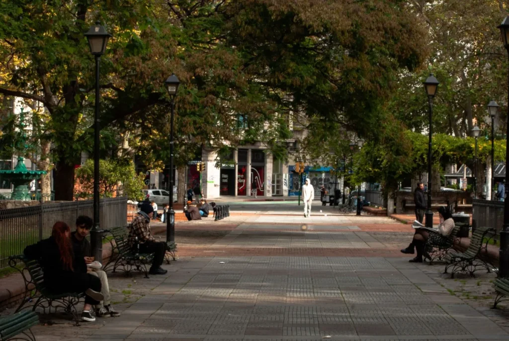 Praca arborizada com bancos e pessoas sentadas no centro da cidade