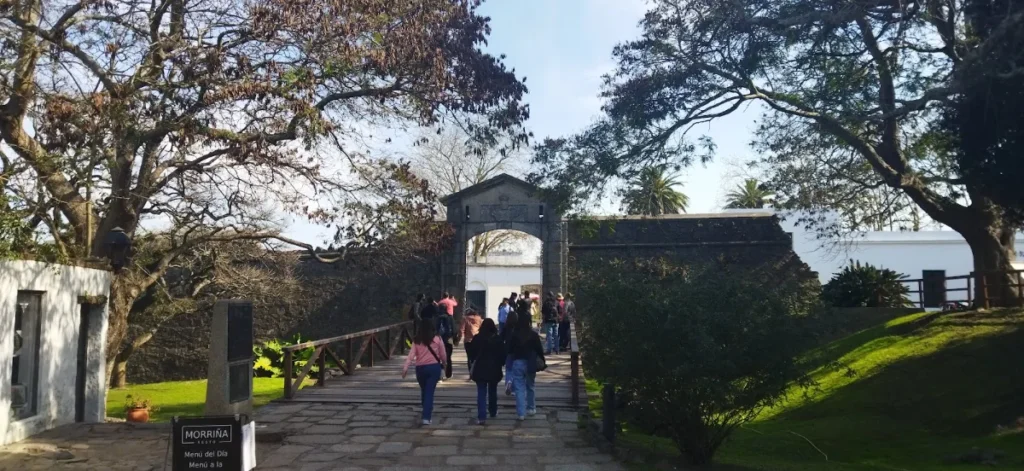 Visitantes atravessando a ponte de madeira sob o arco da Porta do Campo