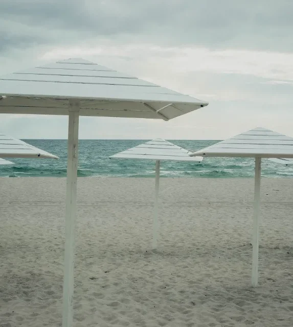 Guarda-sois brancos alinhados na areia diante do mar calmo