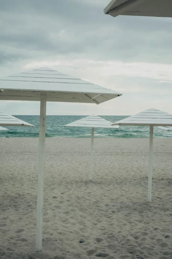 Guarda-sois brancos alinhados na areia diante do mar calmo