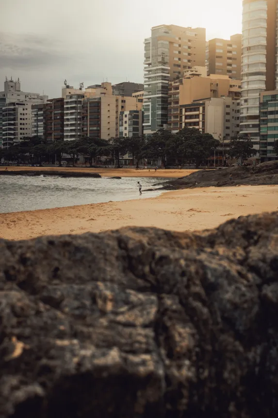 Faixa de areia entre pedras com prédios residenciais à beira-mar