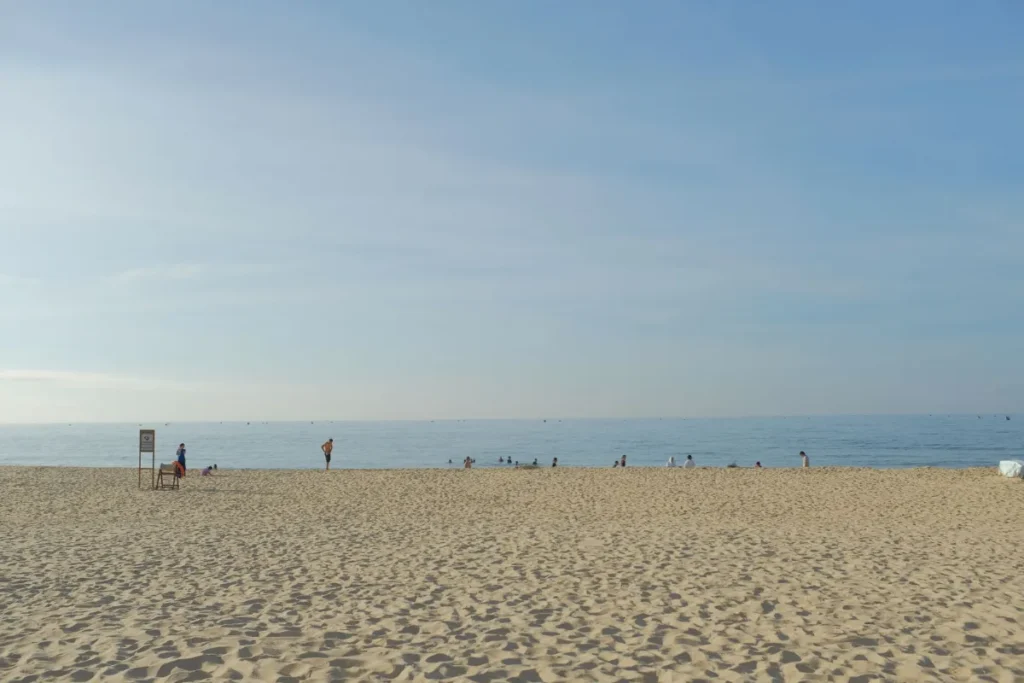 Praia larga e aberta com poucos banhistas ao longe