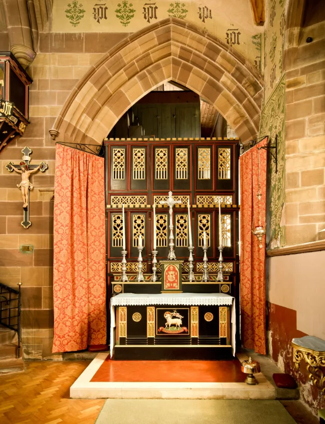 Altar de igreja sob arco de pedra, com crucifixo na parede lateral