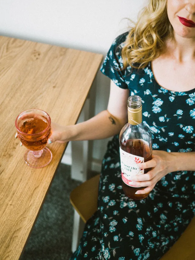 Taça de vinho rosé servida ao lado da garrafa sobre mesa de madeira