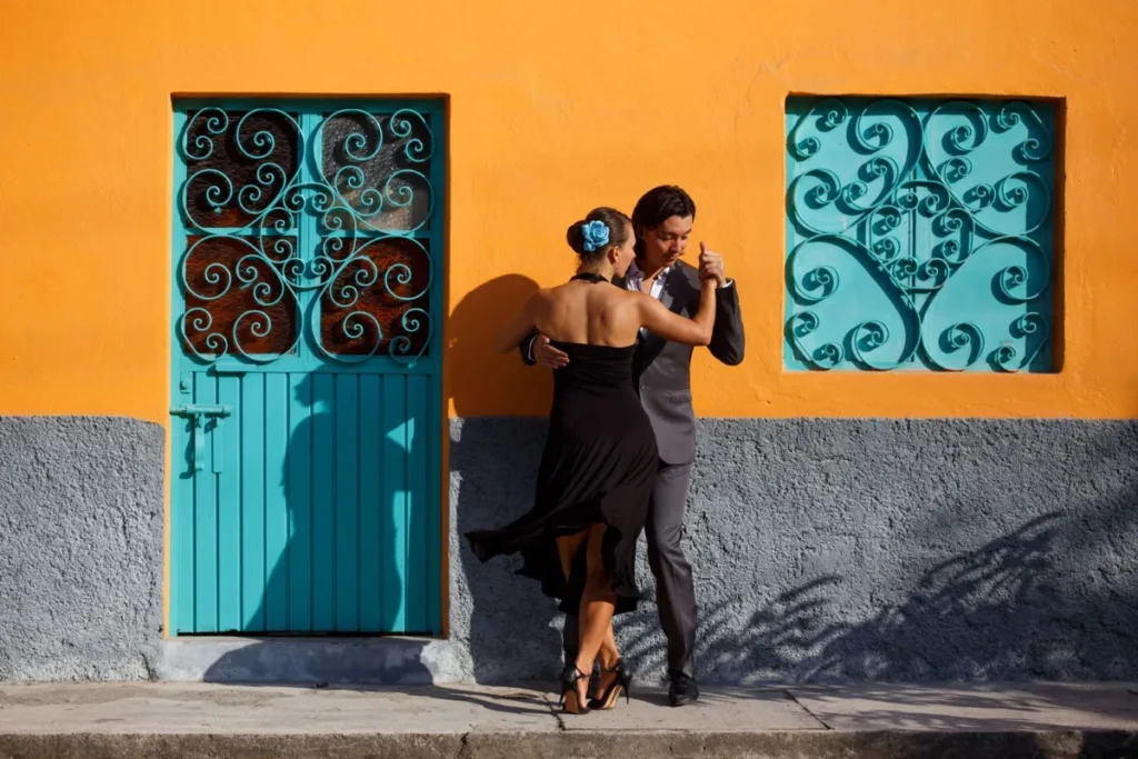 Casal dançando tango na calçada diante de uma parede colorida