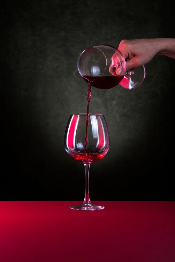 Vinho tinto sendo servido em taça sobre fundo escuro