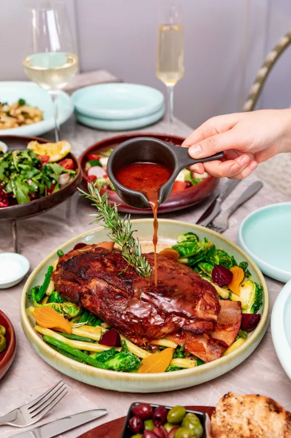 Cordeiro assado servido com legumes e tacas de vinho sobre a mesa