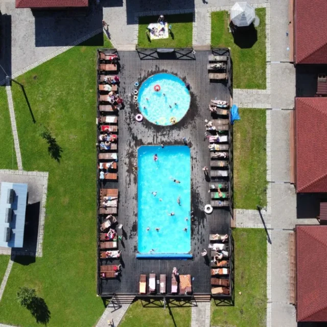 Complexo de piscinas termais visto do alto, cercado por gramado e cabanas
