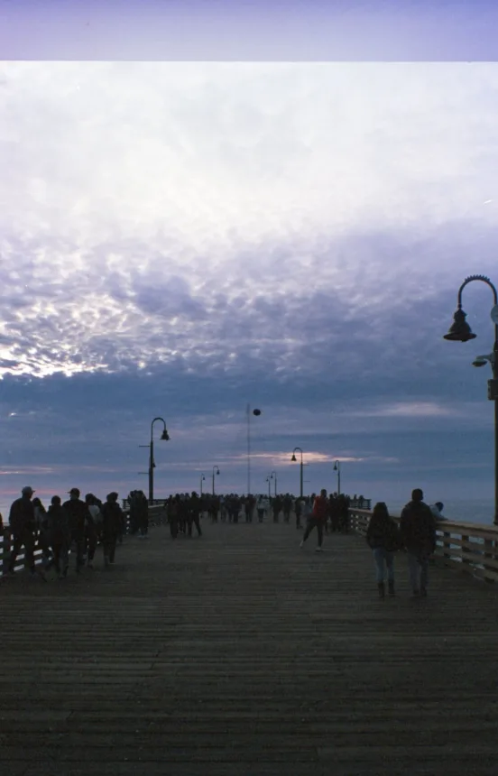 Pessoas caminhando por uma passarela a beira-mar ao por do sol